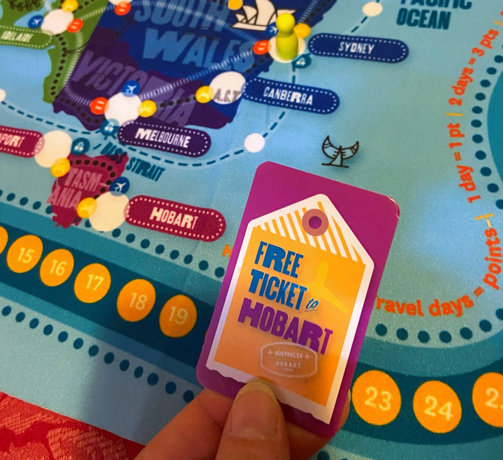 Image of a hand holding a Free Ticket to Hobart card from the tabletop game, TRAVEL BUG