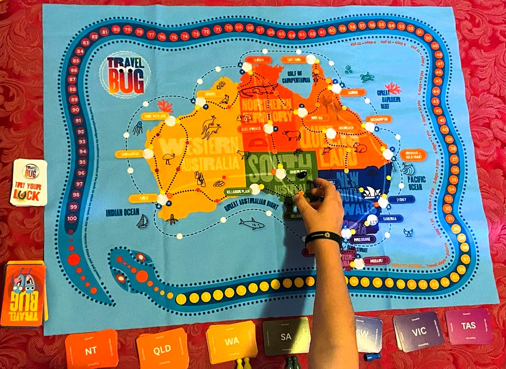 Image of playmat for TRAVEL BUG with a child's hand reaching out to the game