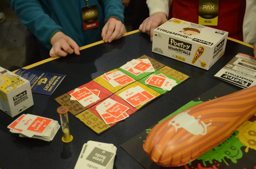 image of a table with the game Poetry for Neanderthals. There are cards set on the table, with a sand timer and an inflatable stick. 