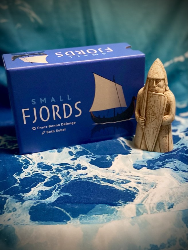 Photo of Small Fjords tabletop game on ocean-pattern background with a stone carving Viking Chess piece