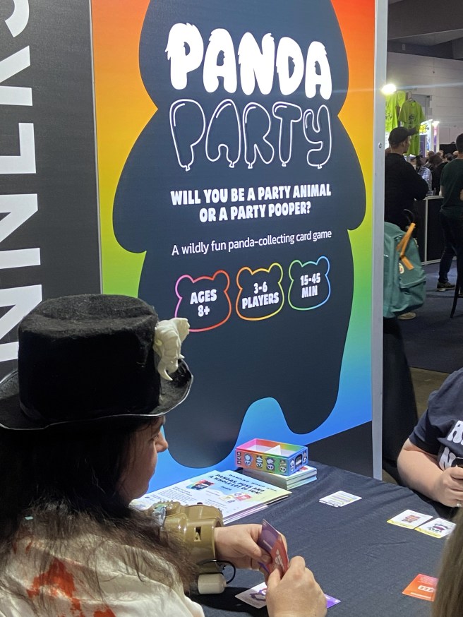 image of a person playing Panda Party wearing a Top Hat in front of the large PAX  Aus 2025 display for the game